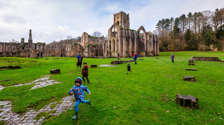 Children running past the ruins at Fountains Abbey and Studley Royal Water Garden, North Yorkshire